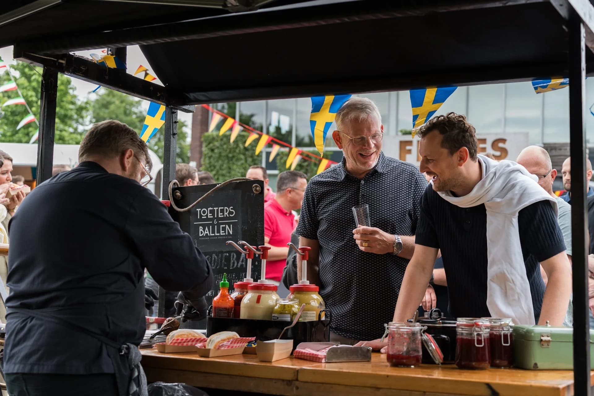 Medewerkers schenken drankjes in achter een buitenbar tijdens het zomerfeest van 4PS.