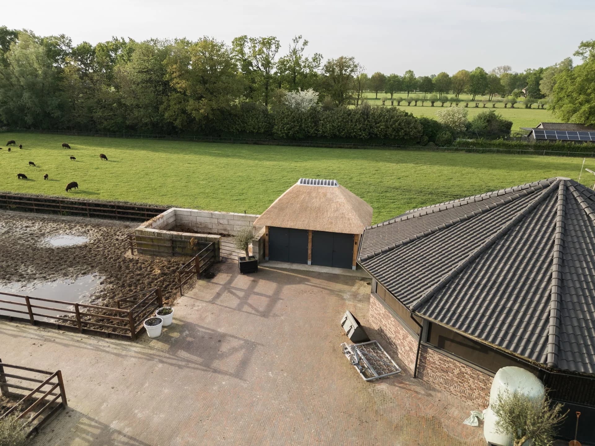 Luchtfoto van een erf met een rietgedekte garage en weiland.
