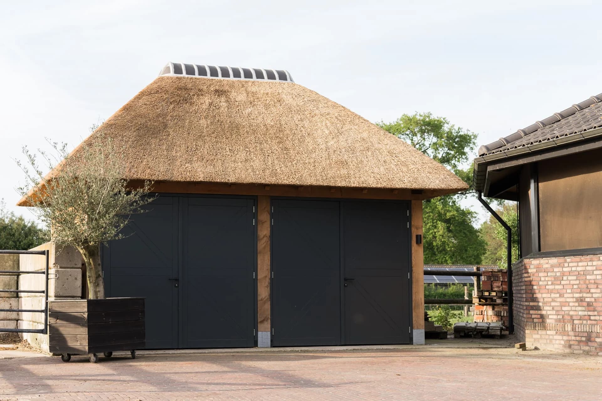 Vrijstaande garage met donkere deuren en een rieten dak.