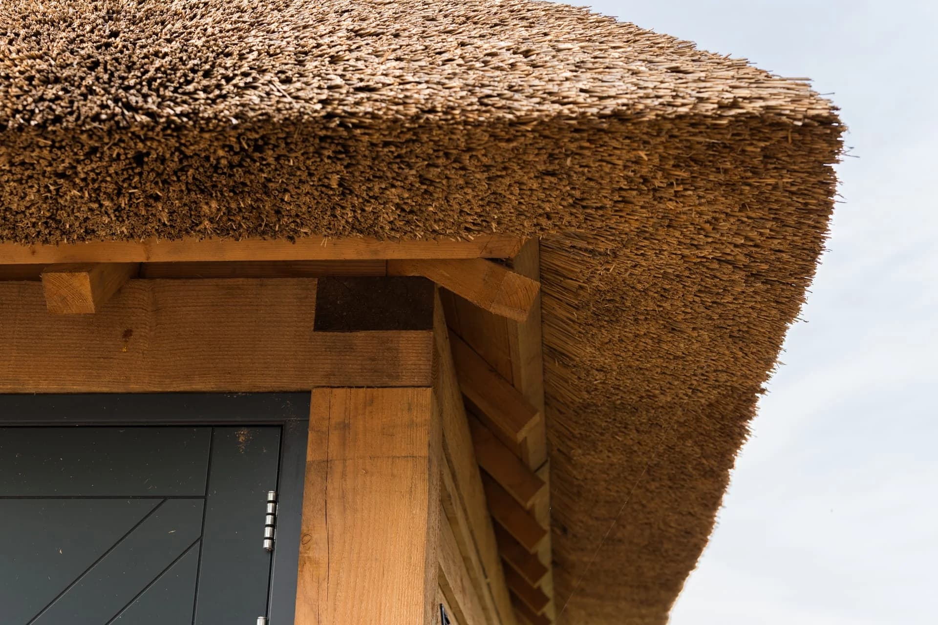 Detail van de rieten dakrand en houten constructie van een garage.