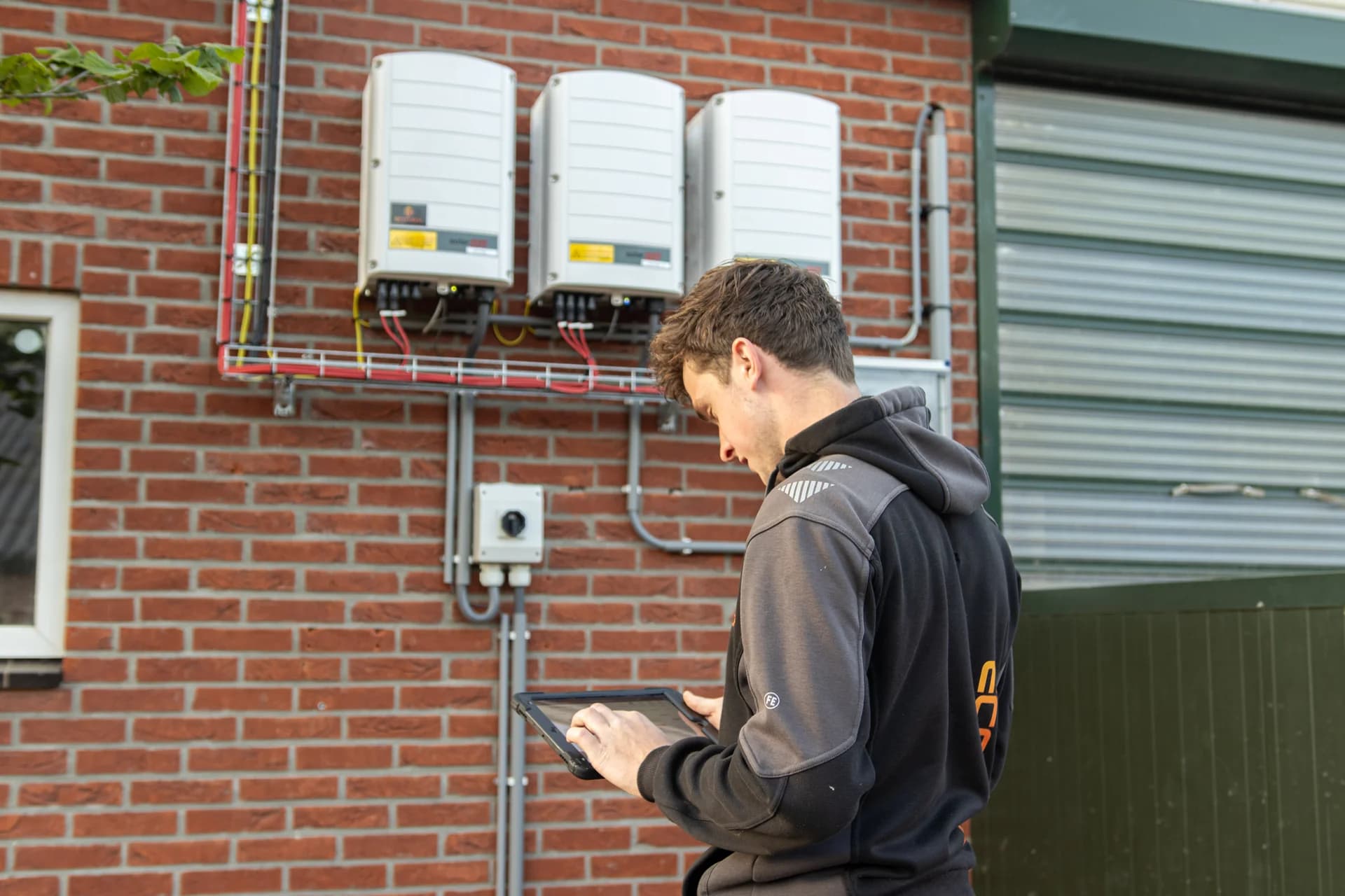 EcoTech-medewerker gebruikt een tablet bij omvormers aan een gevel.