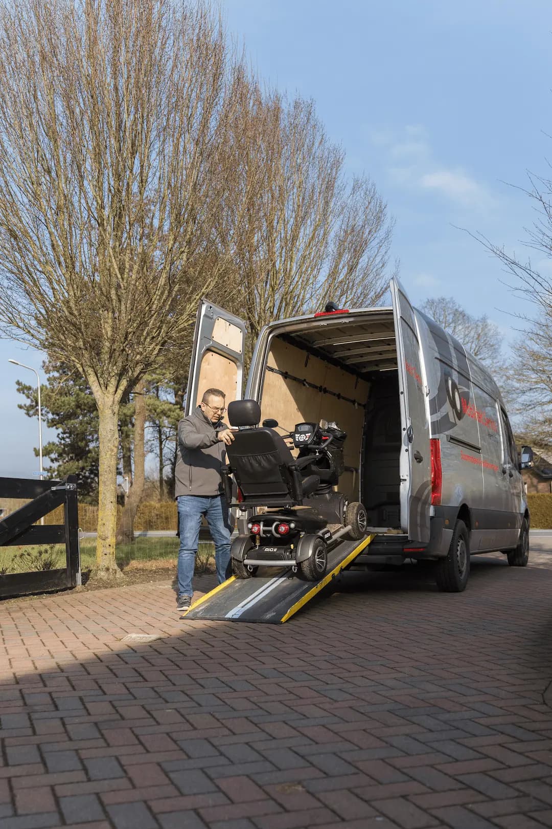 Bestelbus met open achterdeuren en laadklep voor het afleveren van een scootmobiel.