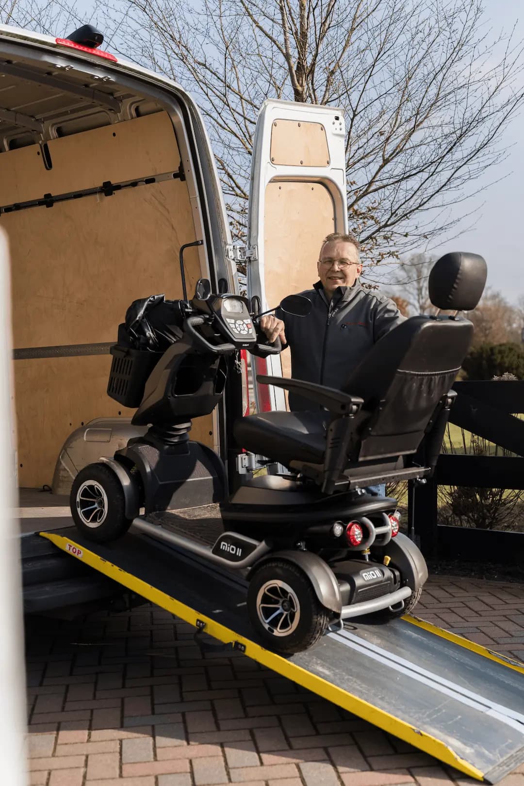 Medewerker bij een scootmobiel op de laadklep van een bestelbus van Mobiliteit Service Harskamp.