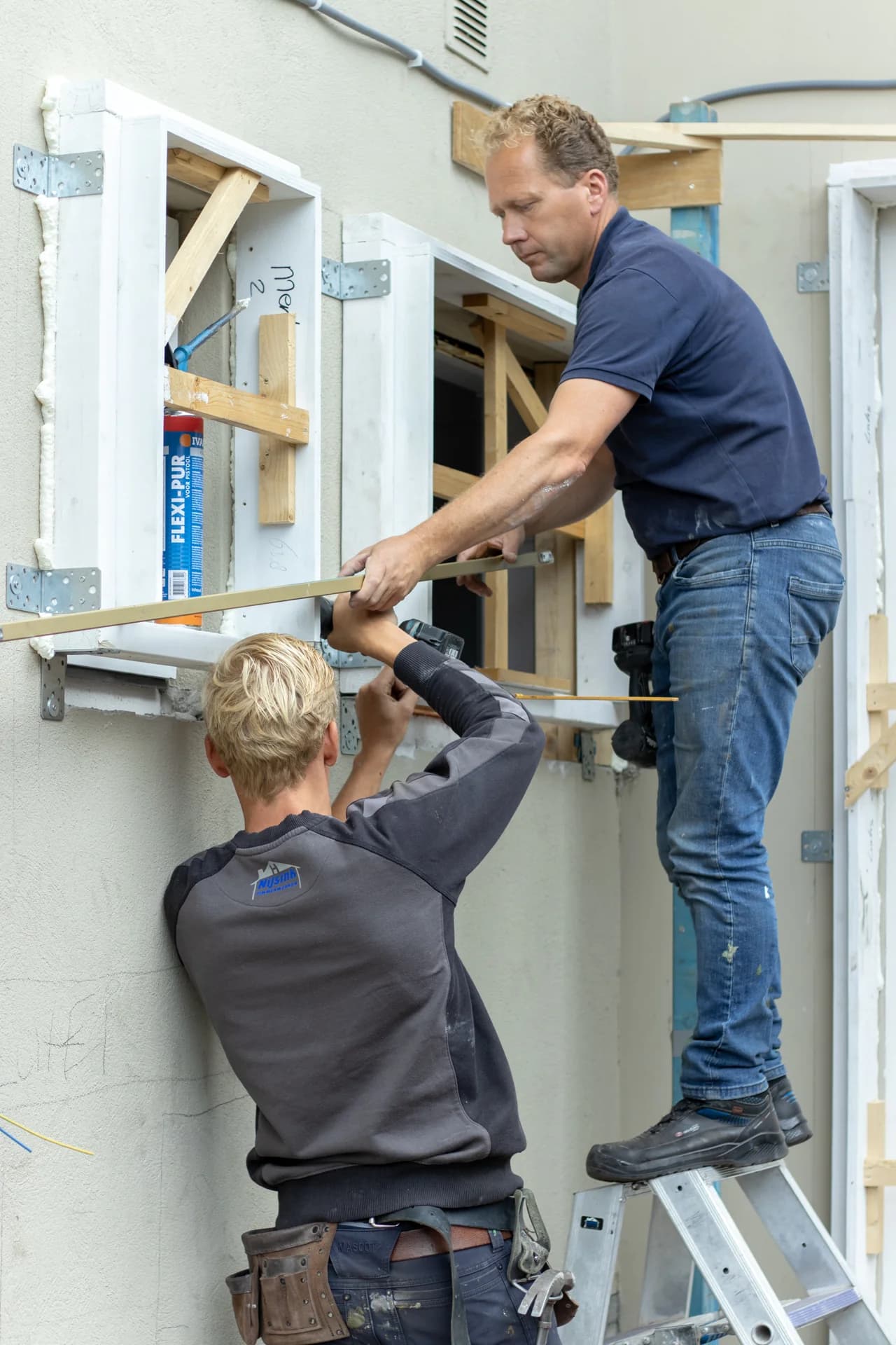 Twee medewerkers van Nijsink plaatsen een raamkozijn tijdens een renovatie.