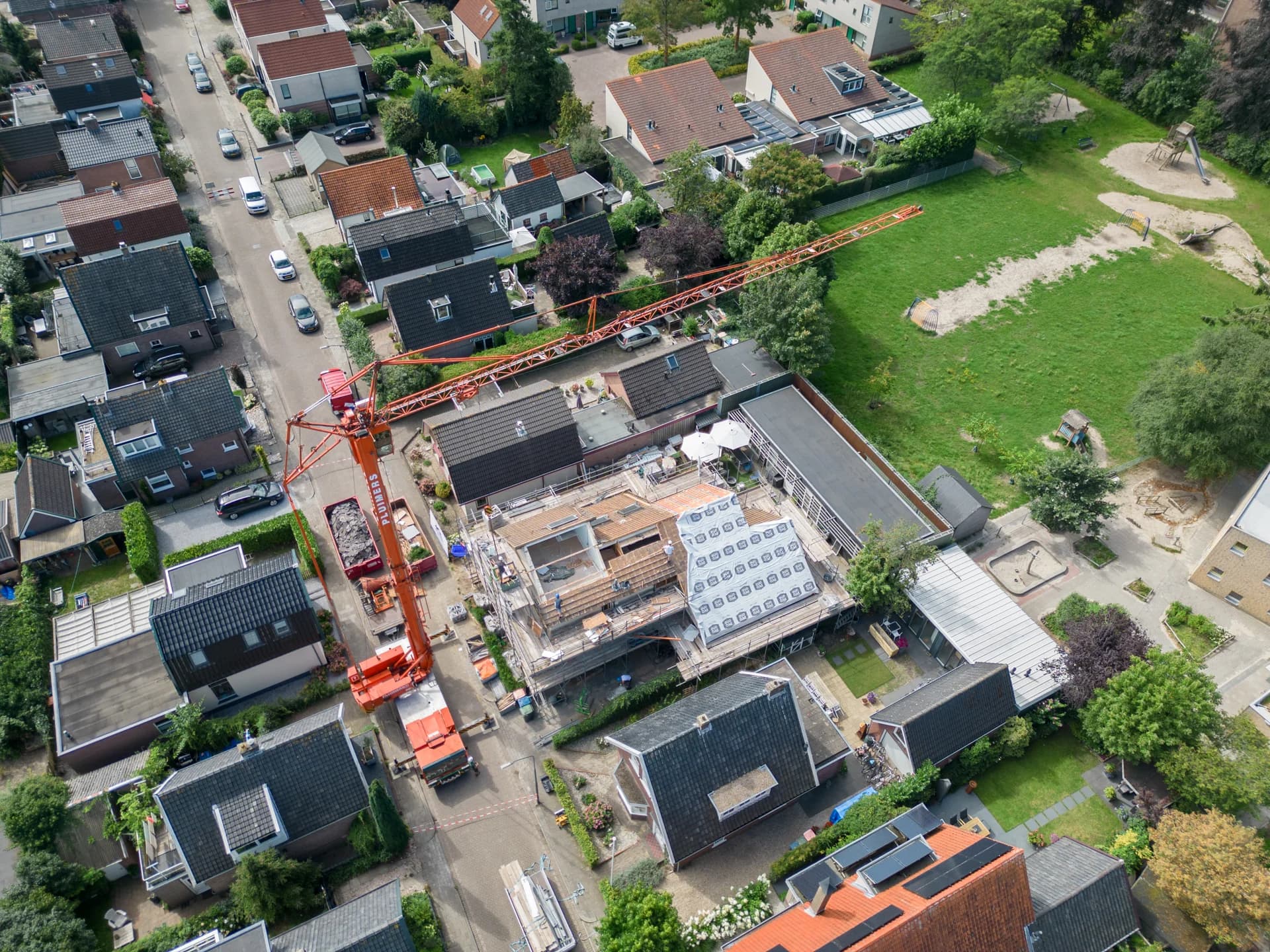 Luchtfoto van een renovatiewoning met steigers en een bouwkraan.