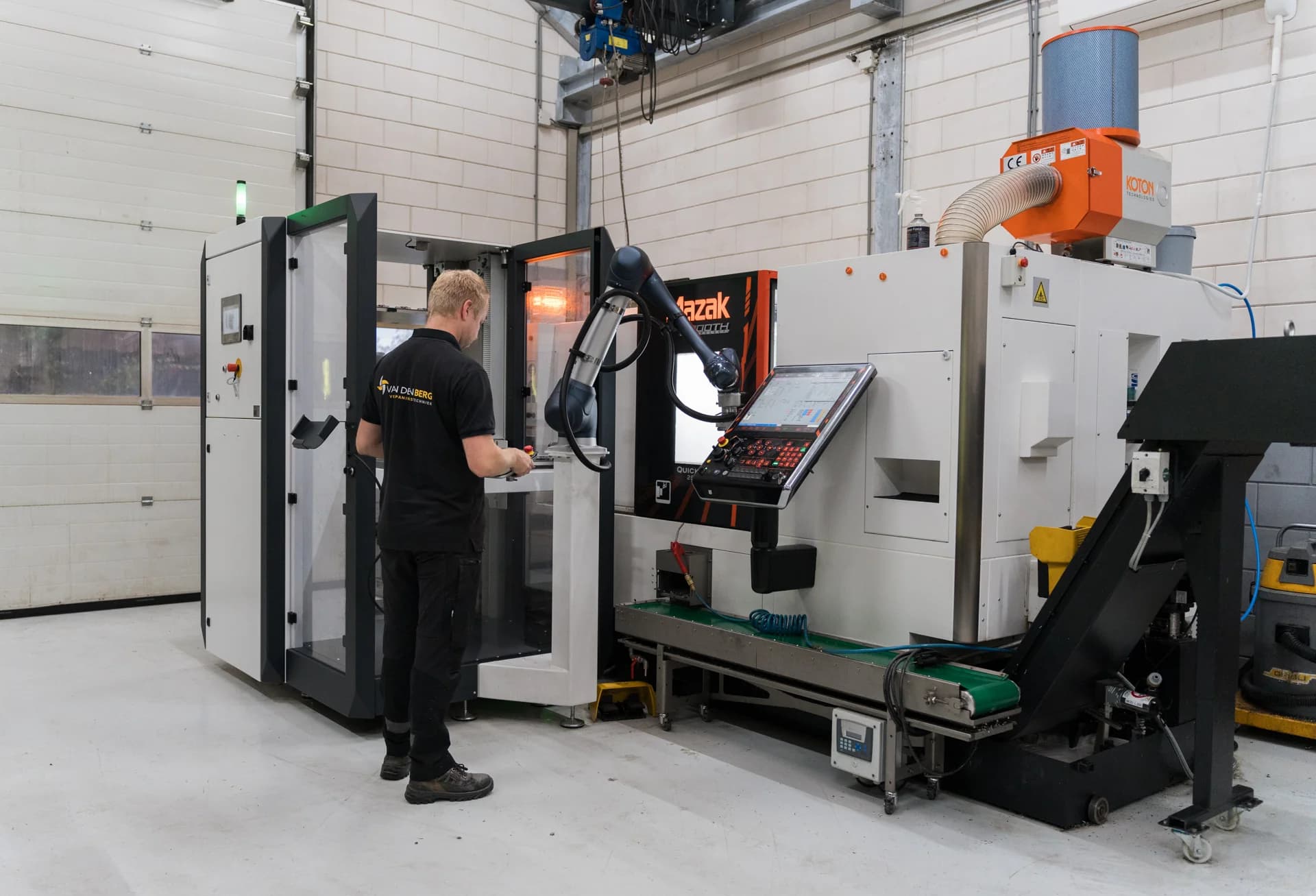 Medewerker werkt bij een CNC-machine met robotarm in de werkplaats.
