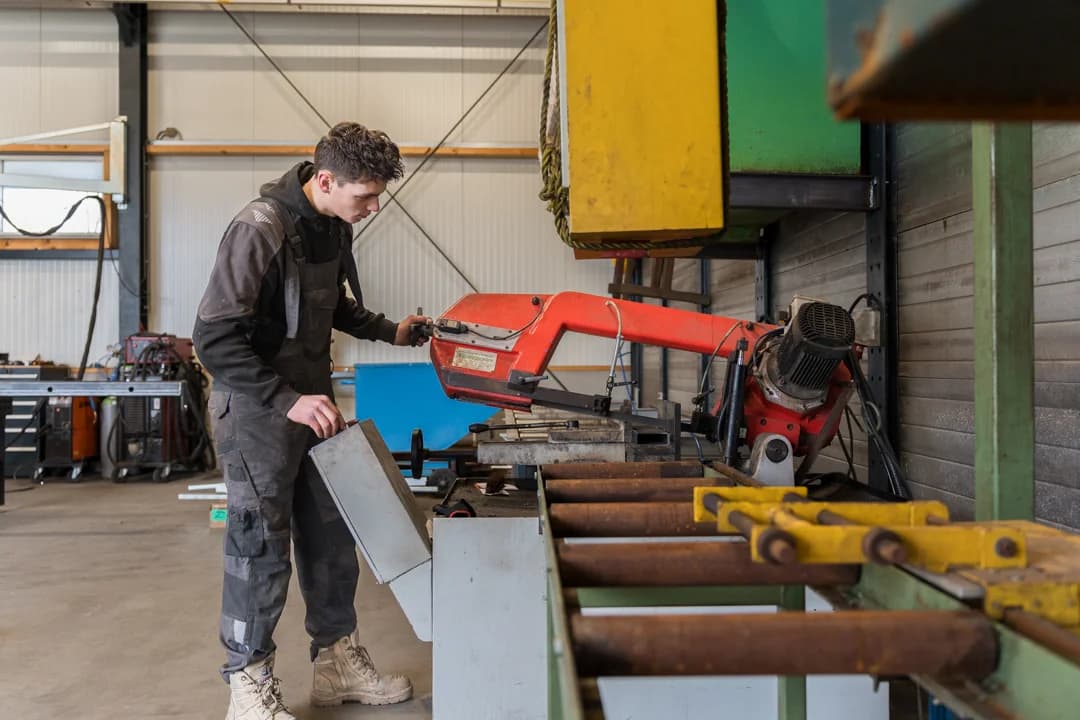 Medewerker zaagt een metalen onderdeel met een zaagmachine.