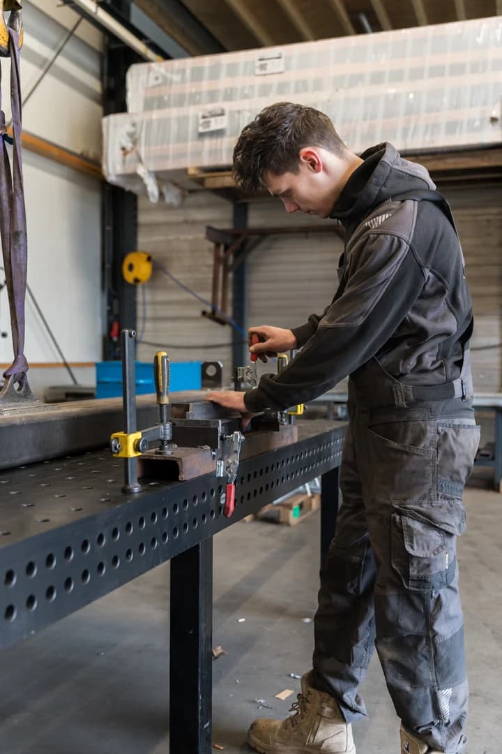 Medewerker bewerkt een metalen onderdeel aan een werkbank.