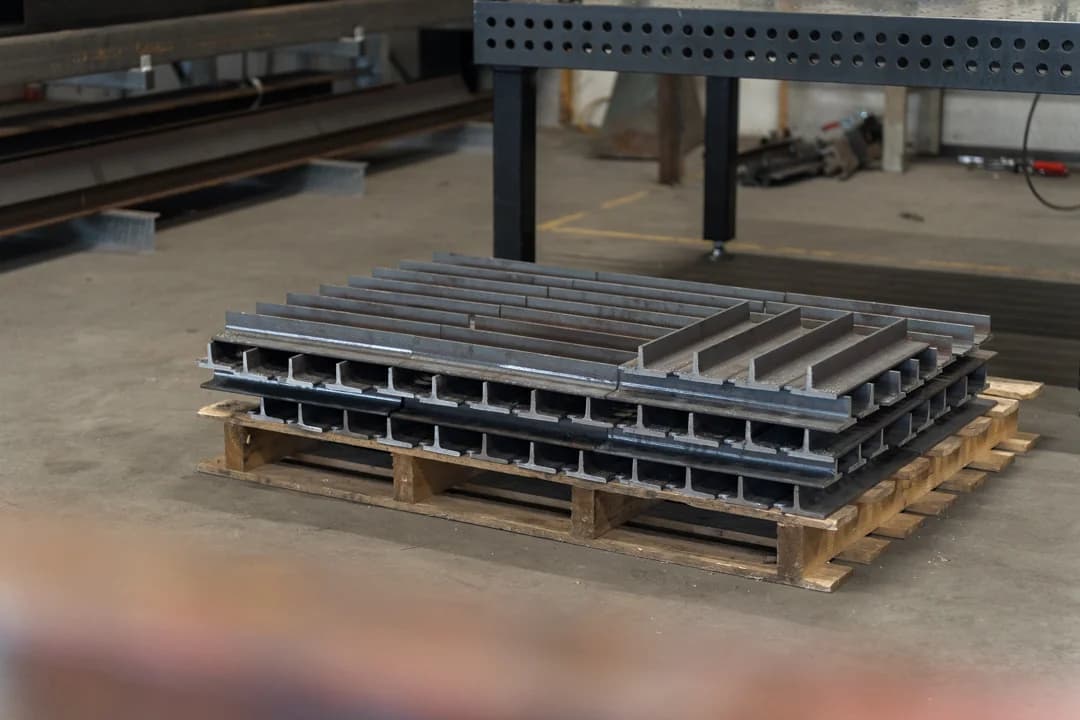 Gestapelde stalen onderdelen op een pallet in de werkplaats.
